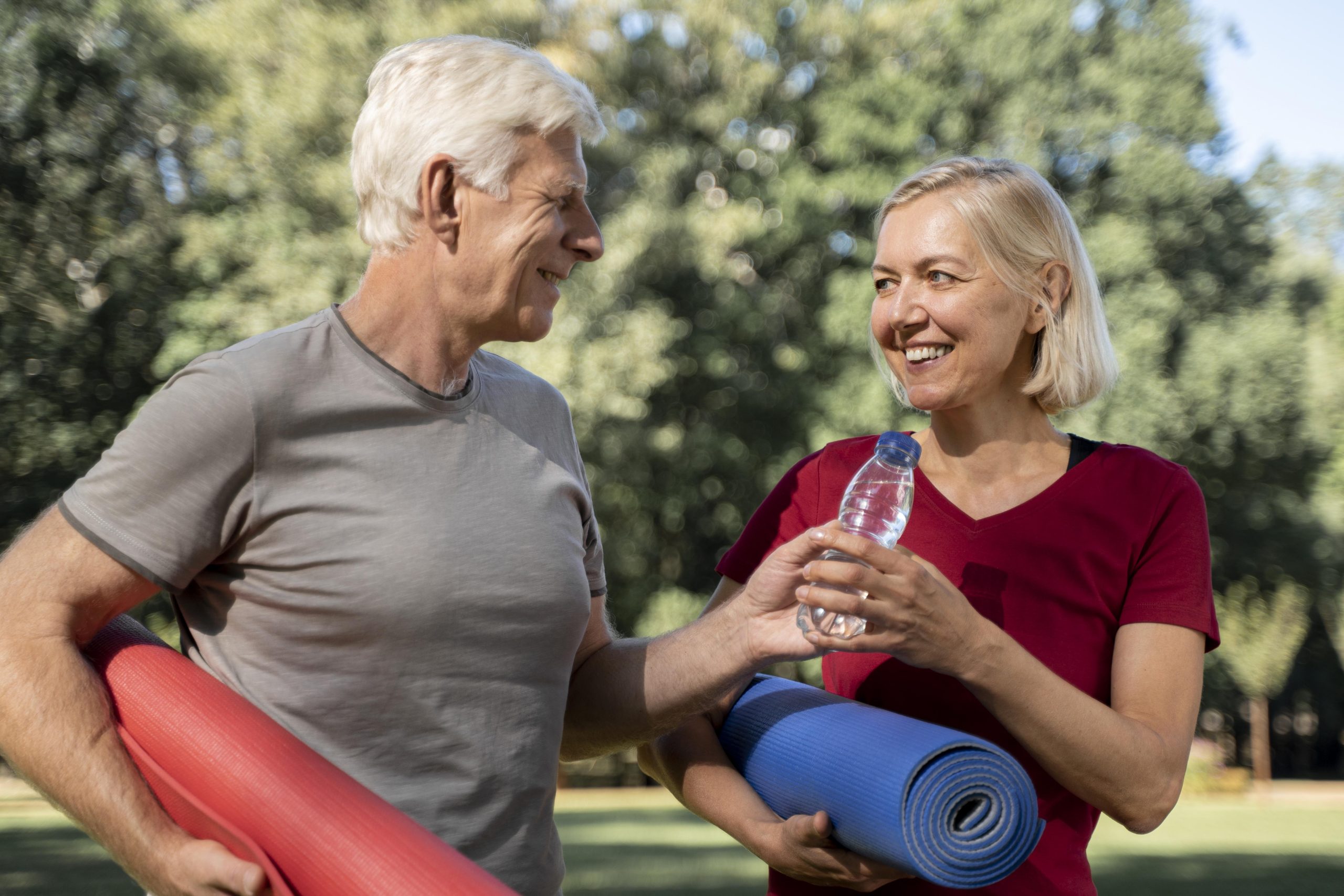 smiley older couple outdoors with yoga mats water bottle
