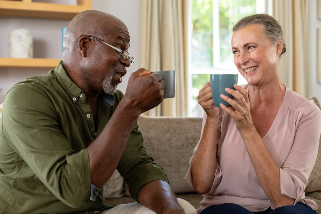 happy-senior-multiracial-couple-having-coffee-while-sitting-sofa-home-unaltered-lifestyle-leisure-retirement-togetherness-drink-refreshment