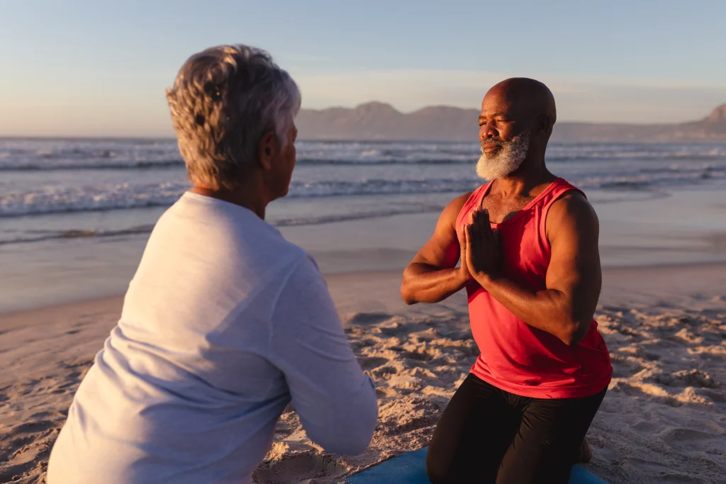 senior-african-american-couple-with-folded-hands-meditating-practicing-yoga-together-beach-fitness-yoga-healthy-lifestyle-concept